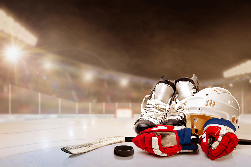 Ice hockey helmet, skates, stick and puck in brightly lit outdoor stadium with focus on foreground and shallow depth of field on background. Deliberate lens flare and copy space. Fictitious background arena created entirely in Photoshop.